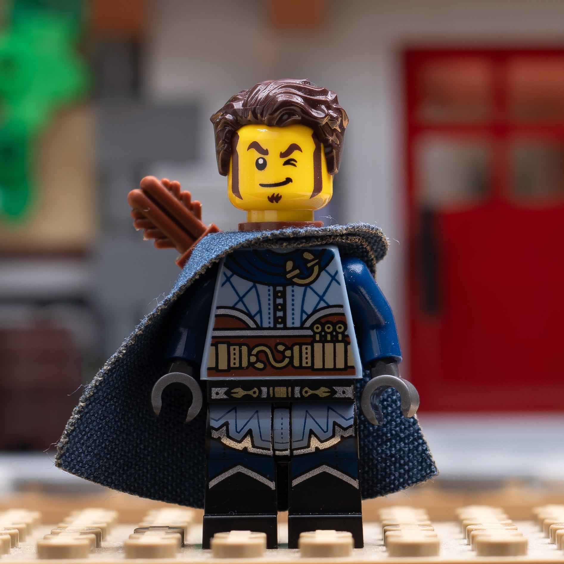 A LEGO minifigure with a blue outfit and cape on a blurred background