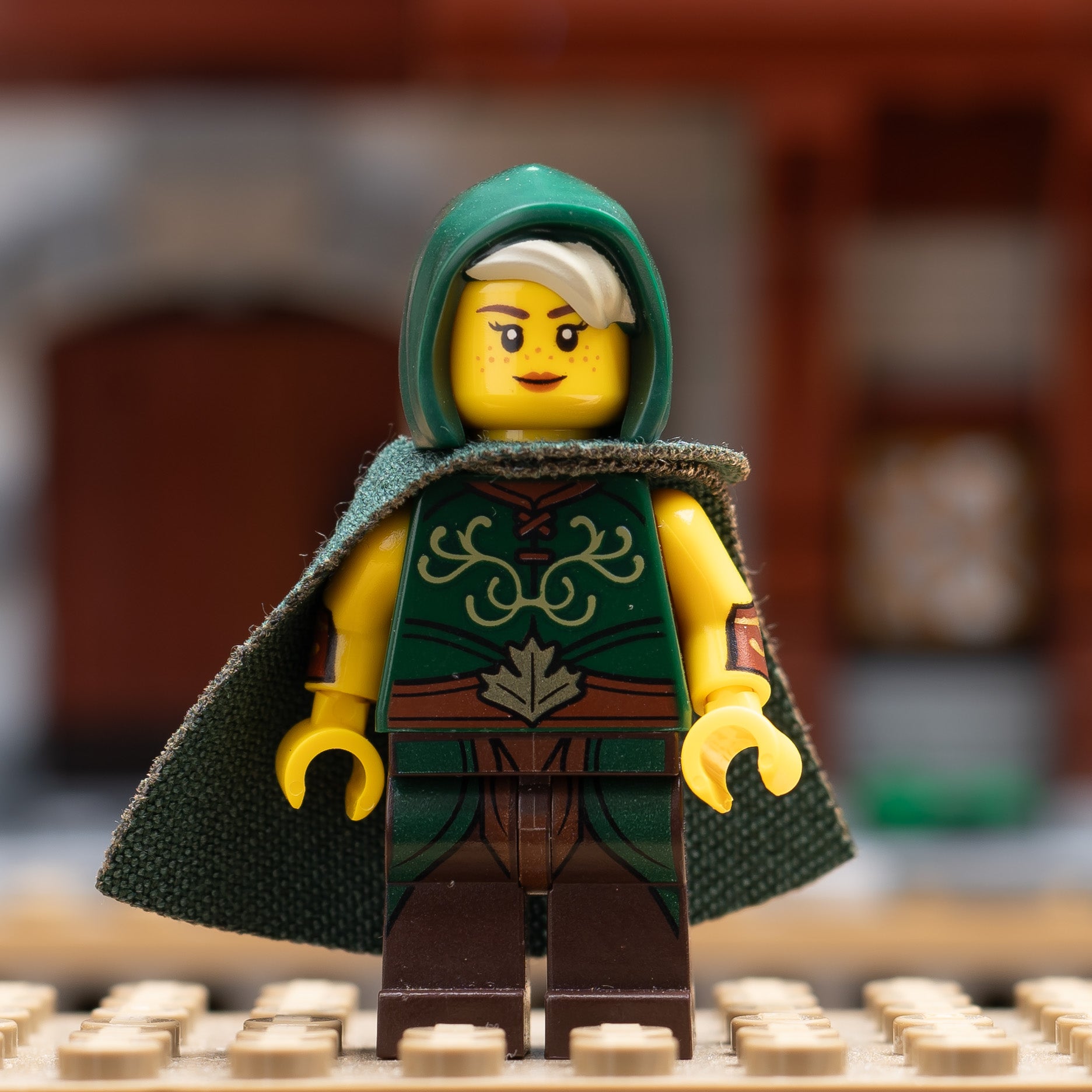 A LEGO minifigure in a green hooded cloak with a blurred background